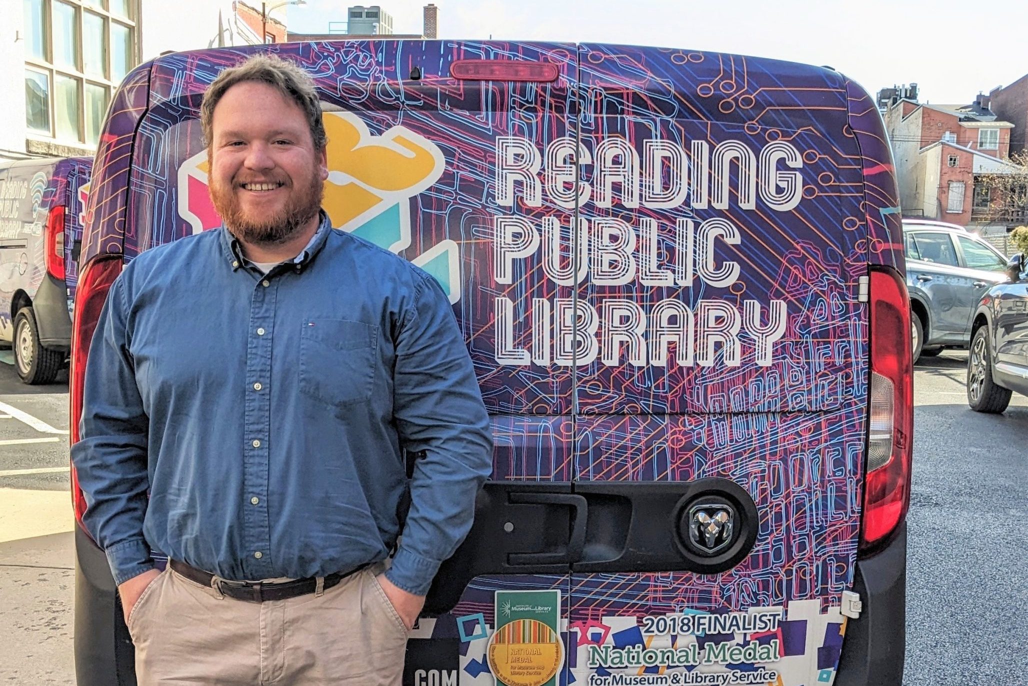 Senior Outreach Coordinator standing next to the Reading Public Library Mobile Tech Van outdoors.