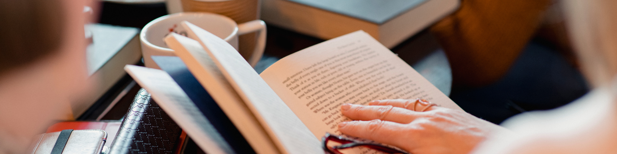 book in woman's hand at a table.